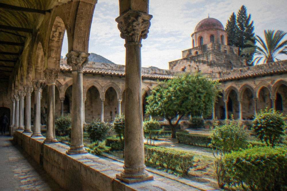 An arcaded cloister with slender columns and a small garden courtyard in Palermo