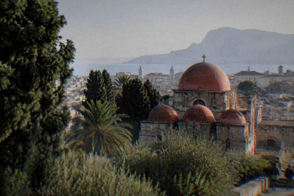 Red domes of a small church rising above trees in the historic centre of Palermo