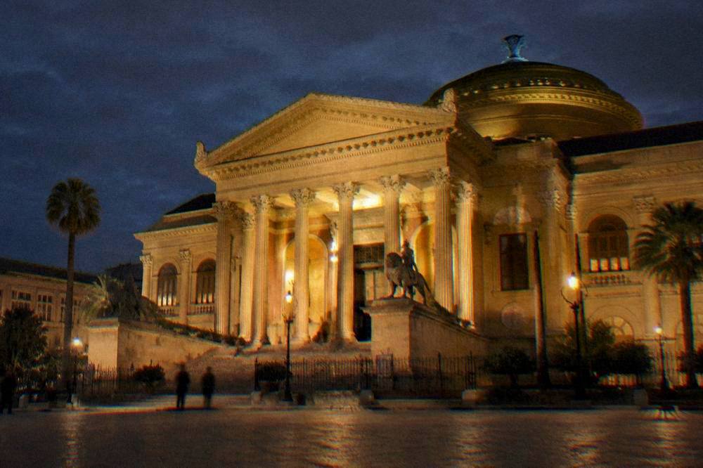 The illuminated facade of the Teatro Massimo at night with the portico columns lit up