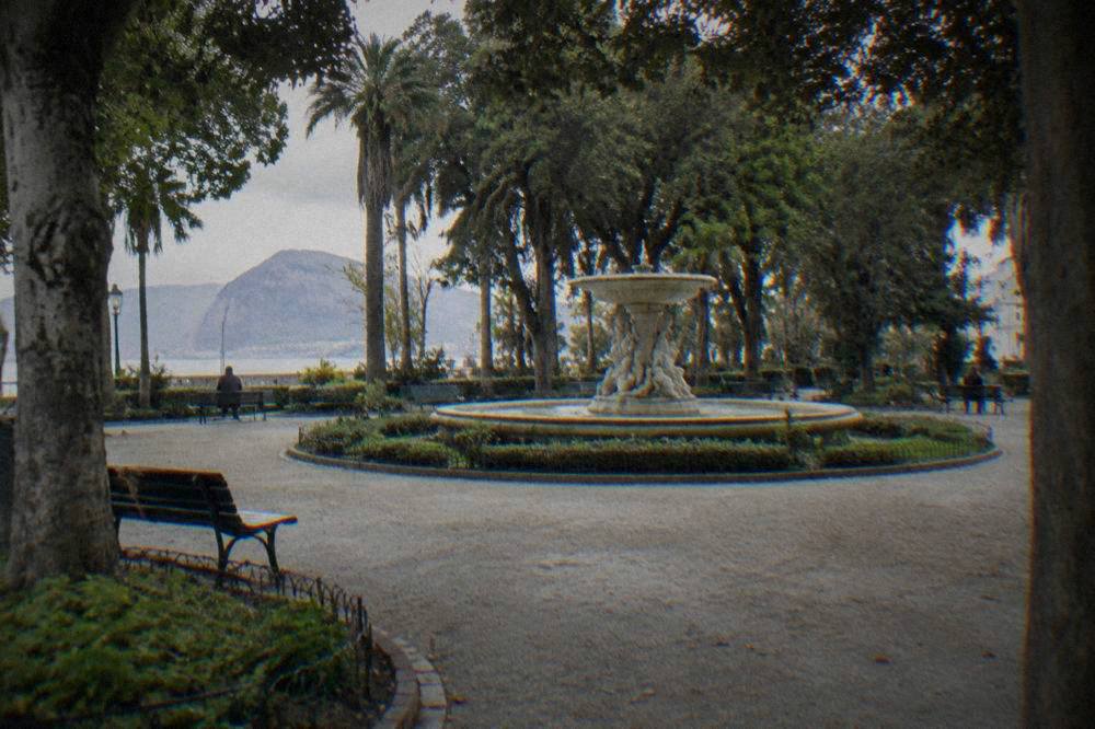A circular plaza in Villa Giulia with a fountain at its centre and benches shaded by tall trees