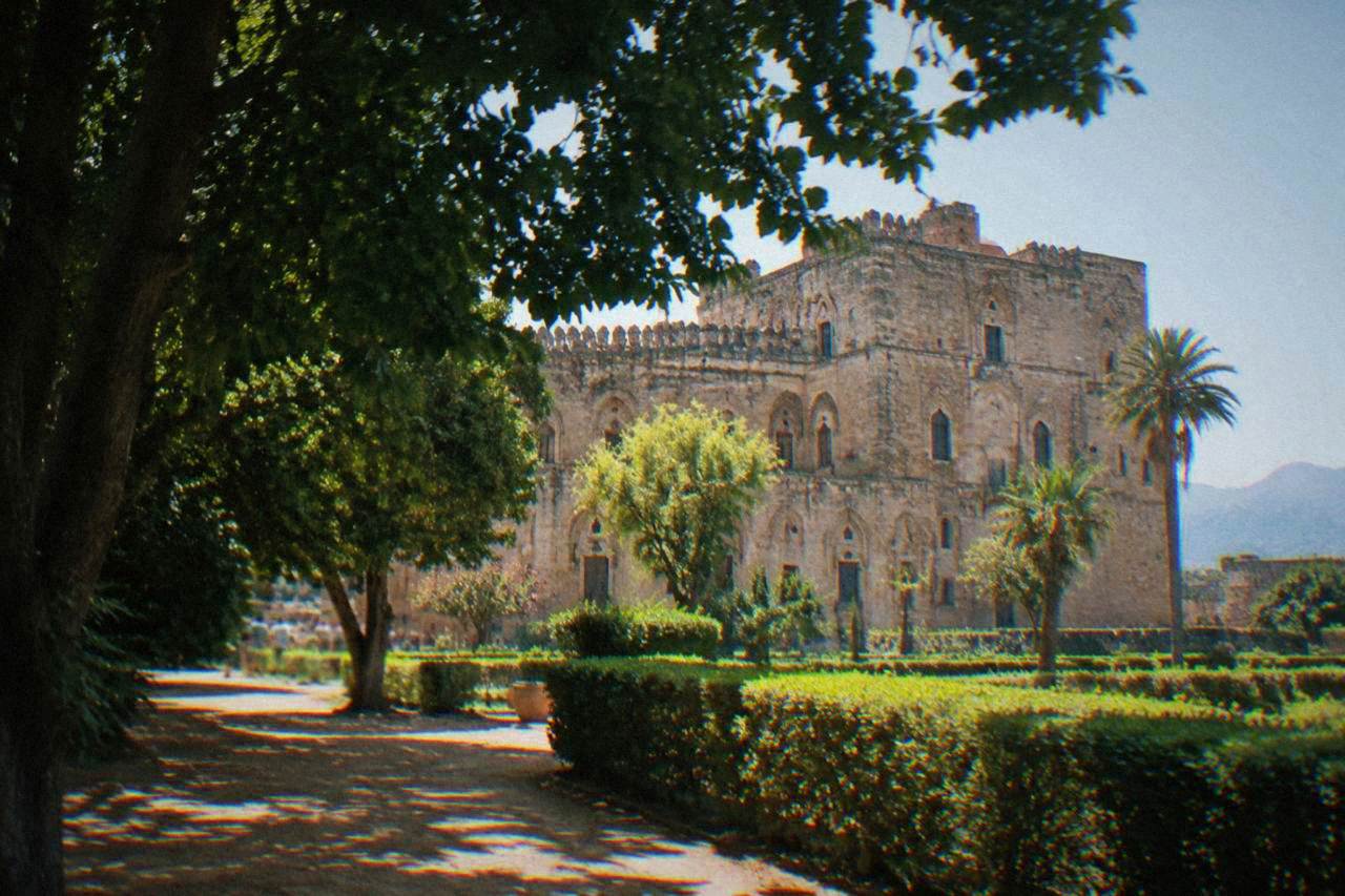 The stone facade of the Zisa Palace in Palermo seen from the gardens in late afternoon light