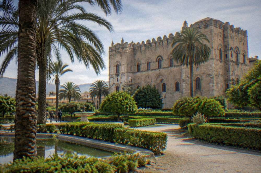 Gardens in front of the Zisa Palace with palm trees and low hedges on a sunny day