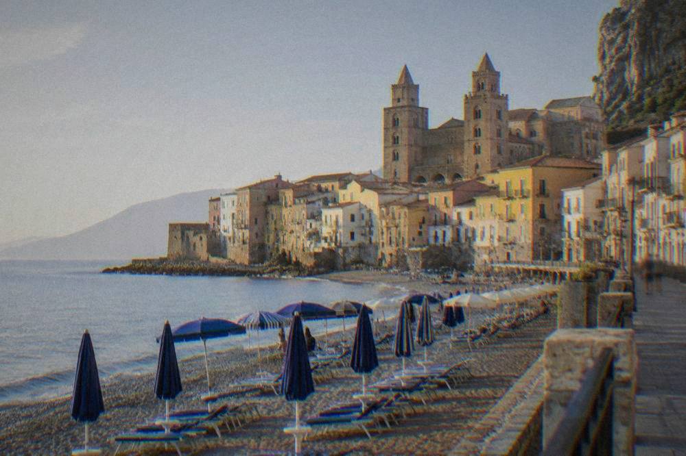The seafront promenade of Cefalu with sunbeds and umbrellas along the water and coloured buildings behind