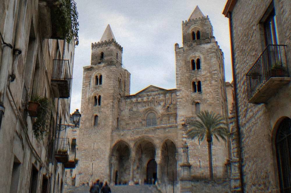 Twin towers and stone facade of Cefalu cathedral seen from the narrow street below