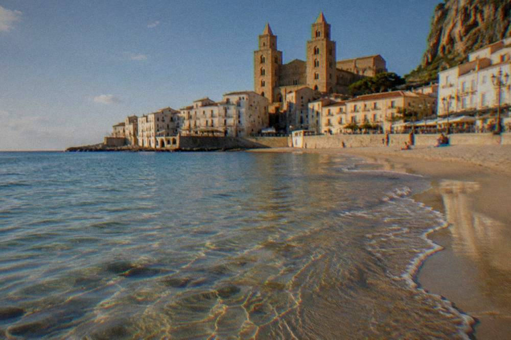 Clear shallow water over sand at the town beach in Cefalu with the promenade and buildings behind