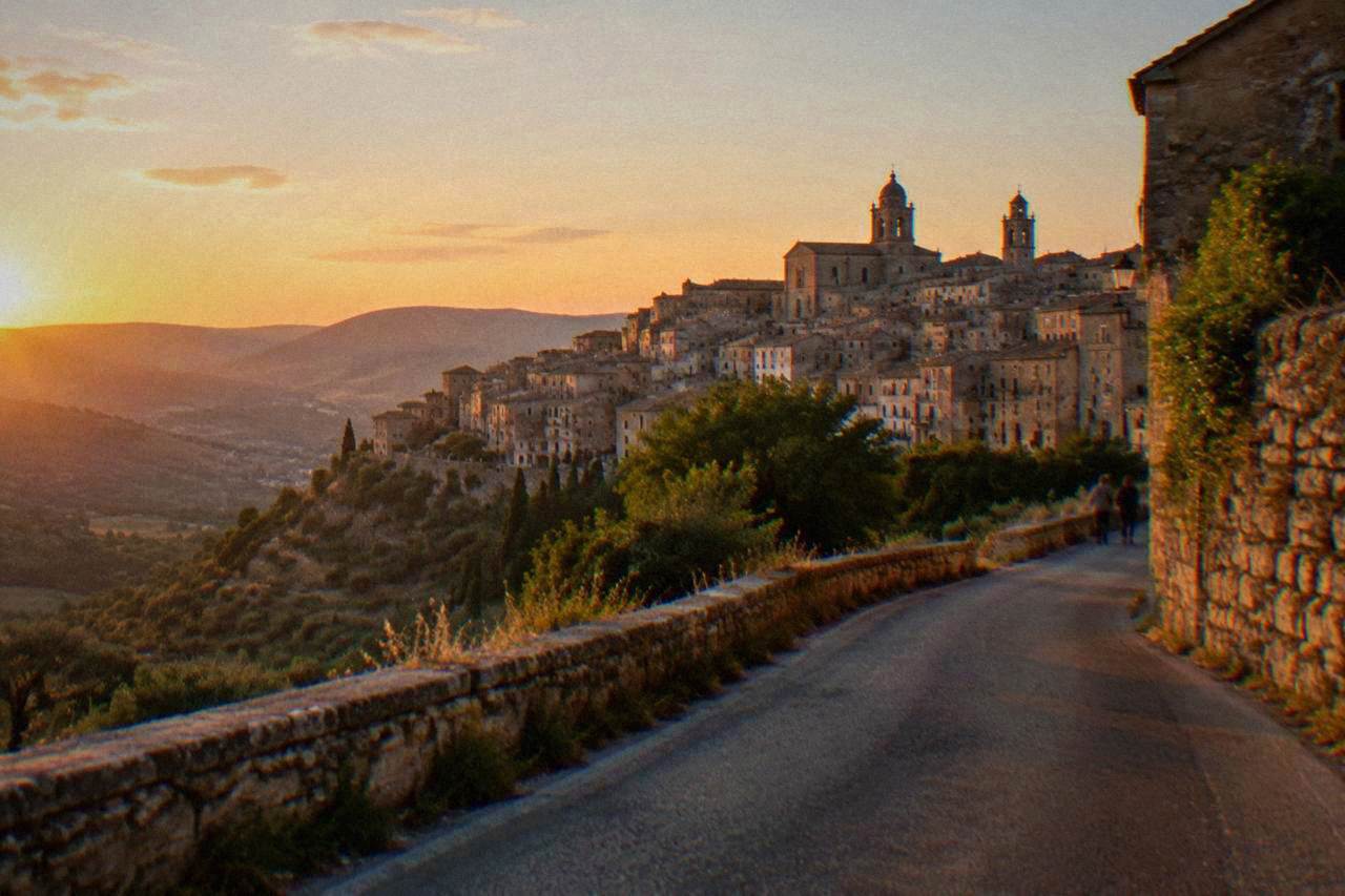 A hill town of stone houses and church towers seen from a winding country road in inland Sicily