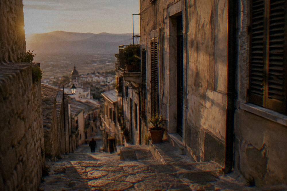 A narrow stone street in a Sicilian hill town with worn steps and shuttered windows