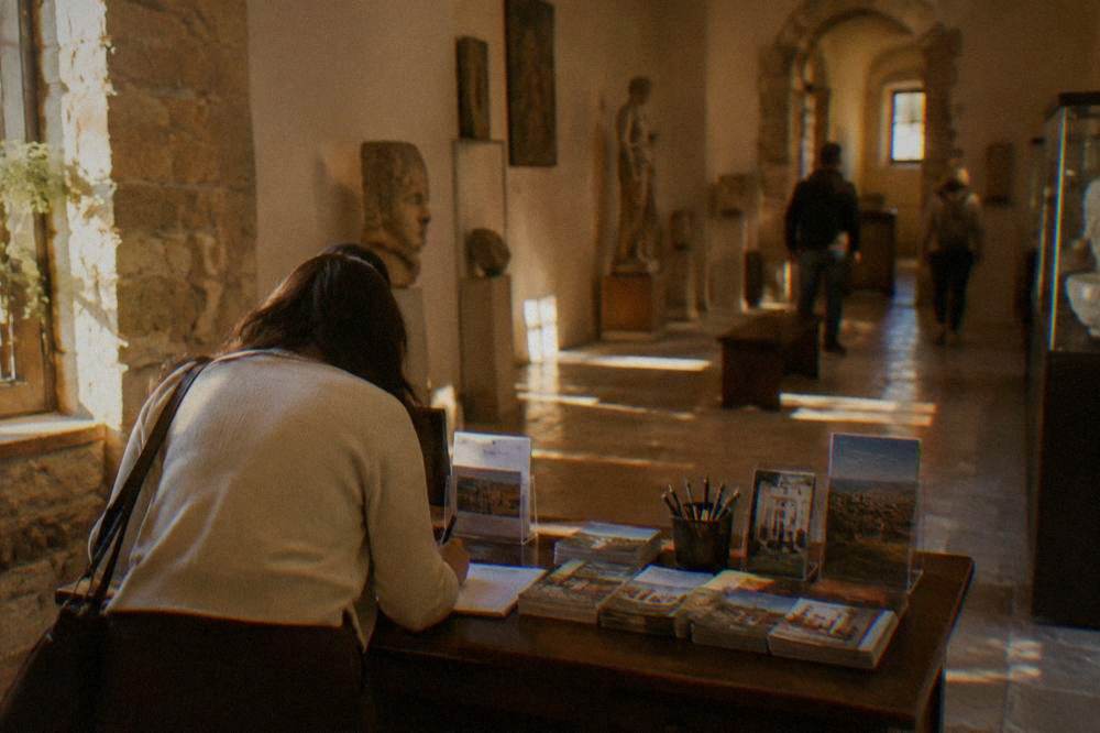 A booking desk in a small Italian museum with leaflets and a visitor signing a form
