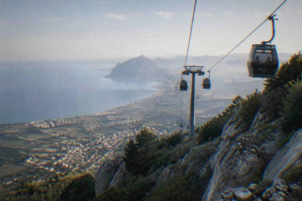 Cable car cabins travelling up a steep mountainside above a coastal plain
