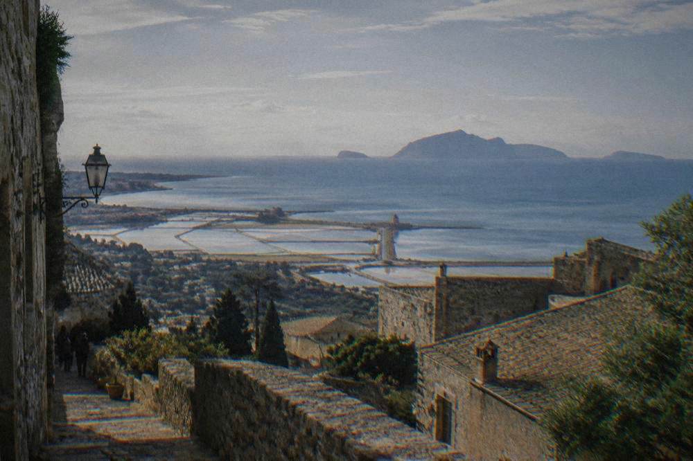 View from a mountain town across coastal salt pans and the sea toward islands