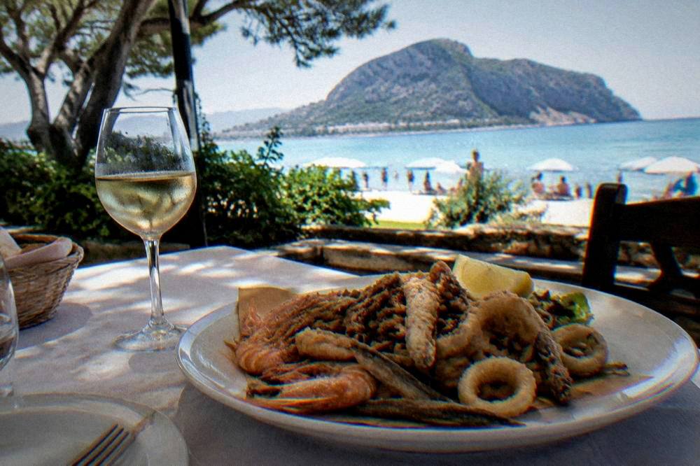 A plate of fried seafood and a glass of white wine on a restaurant table overlooking the sea