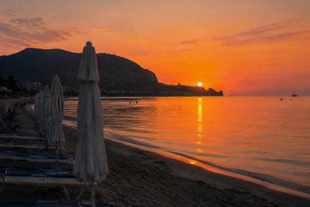Sunset light over a calm bay with beach umbrellas folded and a headland silhouette