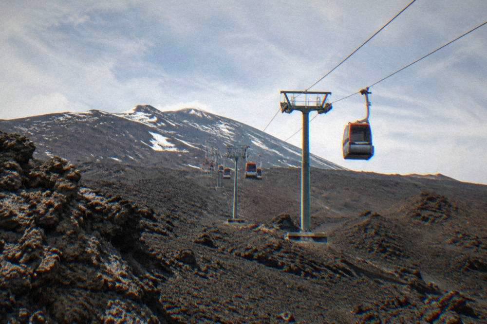 Cable car cabins travelling over black lava fields toward the upper slopes of Etna