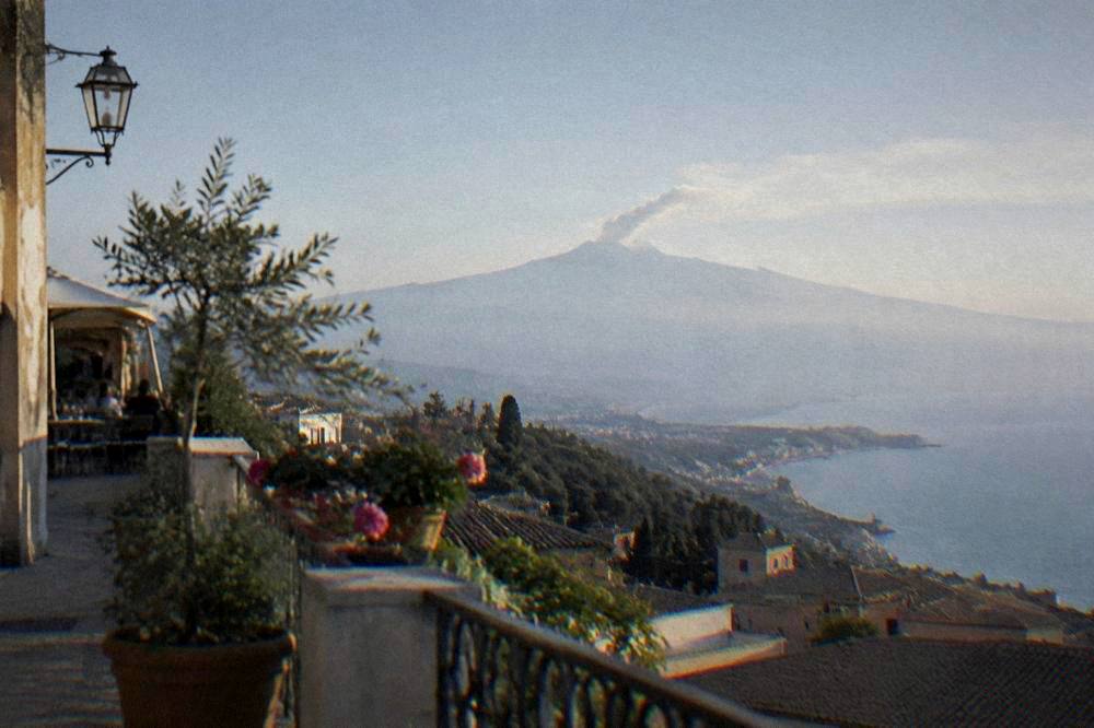 A hillside town terrace overlooking the sea with a large volcano in the distance