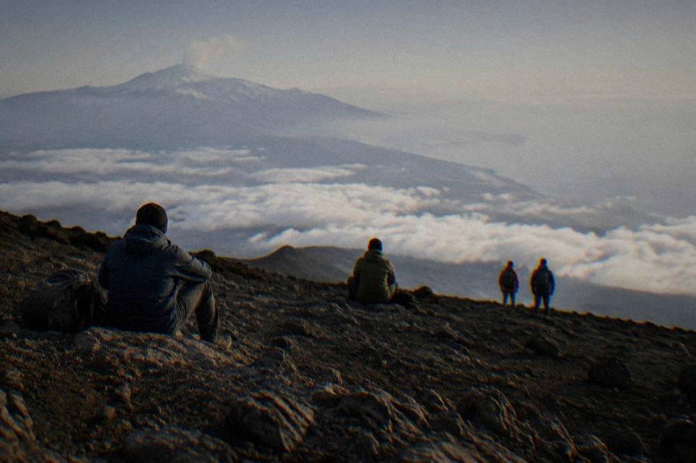 Hikers in windproof jackets and boots resting on a rocky Etna slope above the clouds