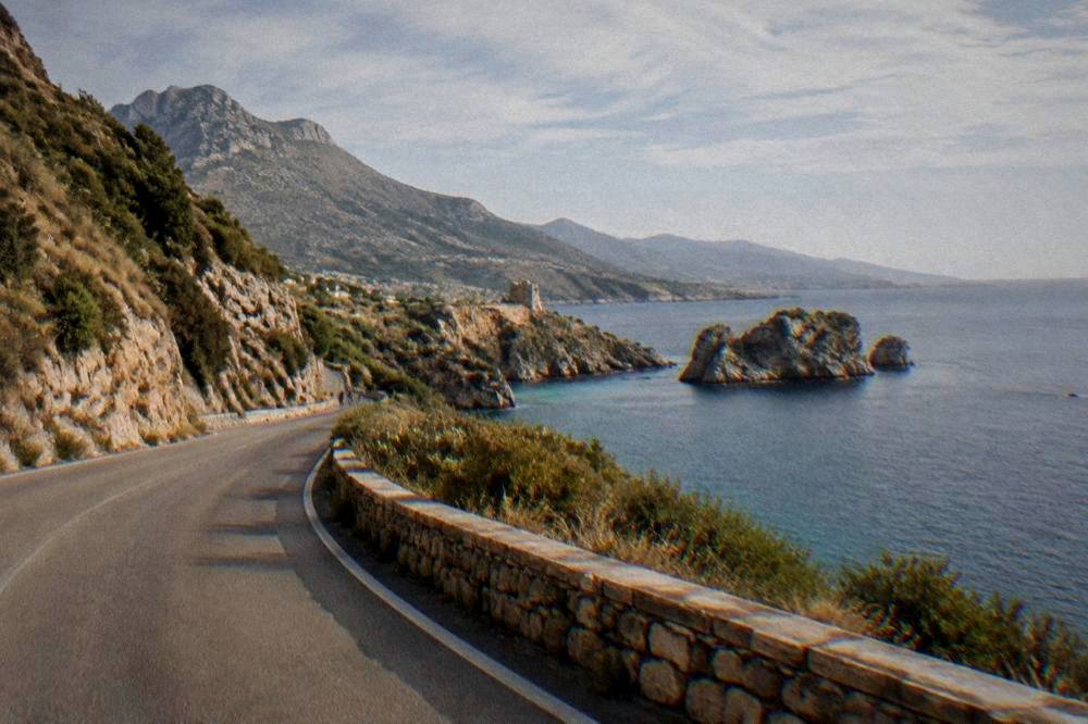 A coastal road curving along a gulf with hills and sea under an open sky