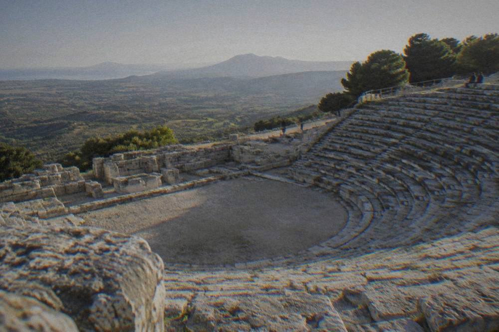 A stone theatre carved into a hillside with views over a green valley in western Sicily