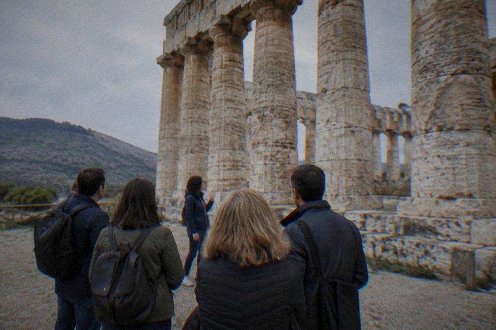 A small group of visitors listening to a guide beside ancient stone columns