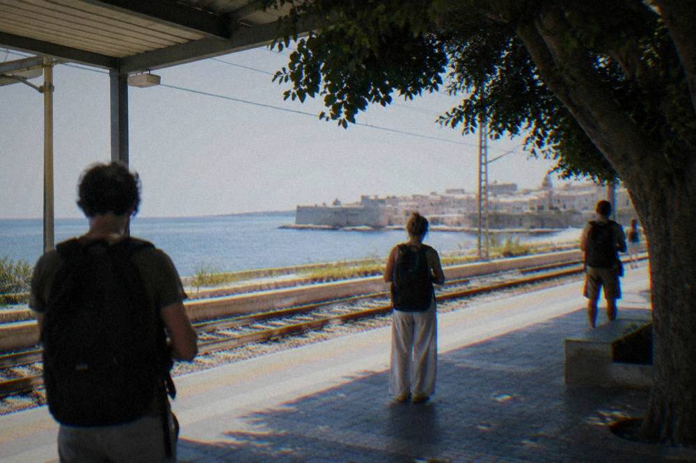 Travellers with backpacks waiting on the platform inside a Sicilian railway station
