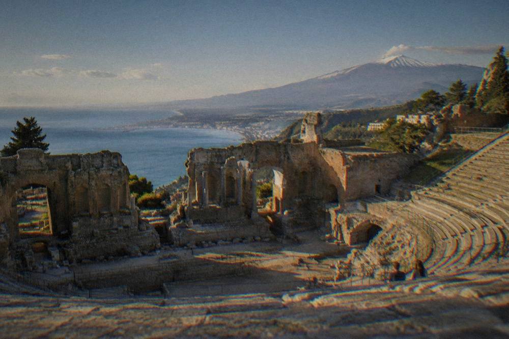 Ancient stone theatre seats at Taormina framing the sea and Mount Etna beyond
