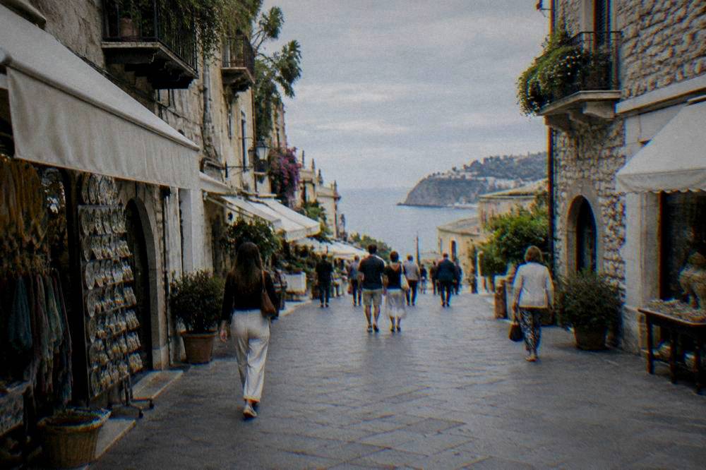 Pedestrian main street in Taormina with stone buildings, awnings and shoppers in daytime
