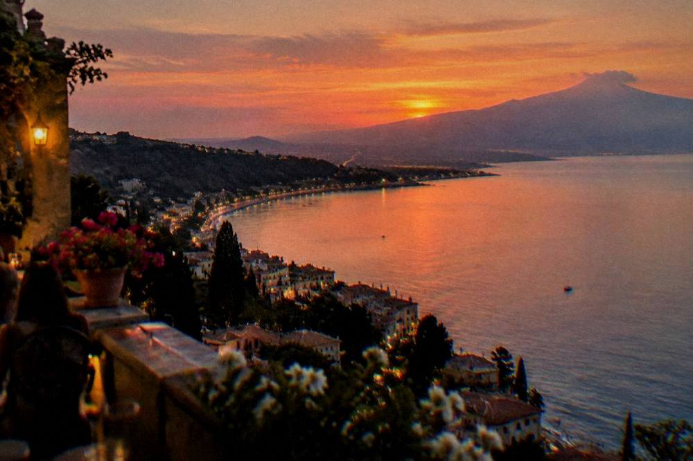 Evening view from a Taormina terrace over the coastline with lights along the bay