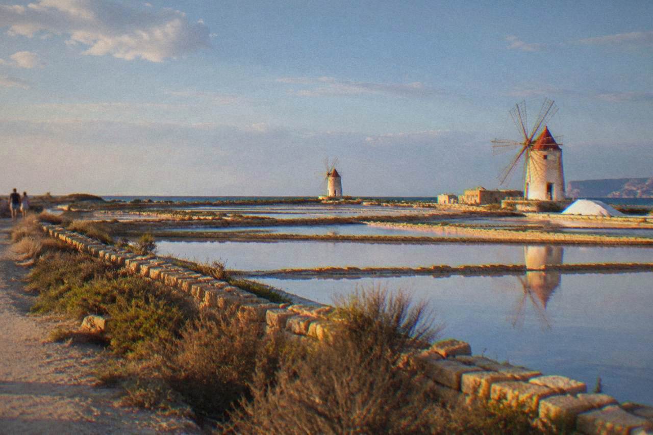 Shallow salt pans stretching to the sea with white windmills under a wide sky