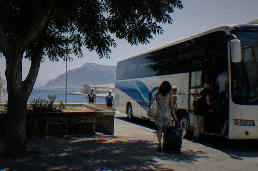 A regional coach parked at a Sicilian roadside station with passengers boarding