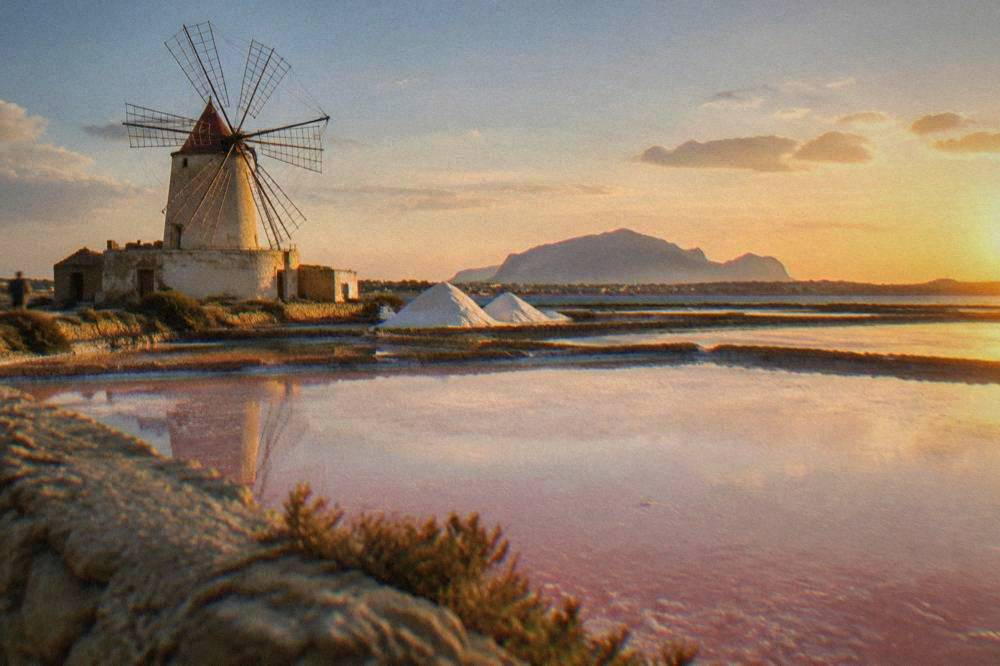Close view of pink and white salt evaporation ponds with a traditional windmill