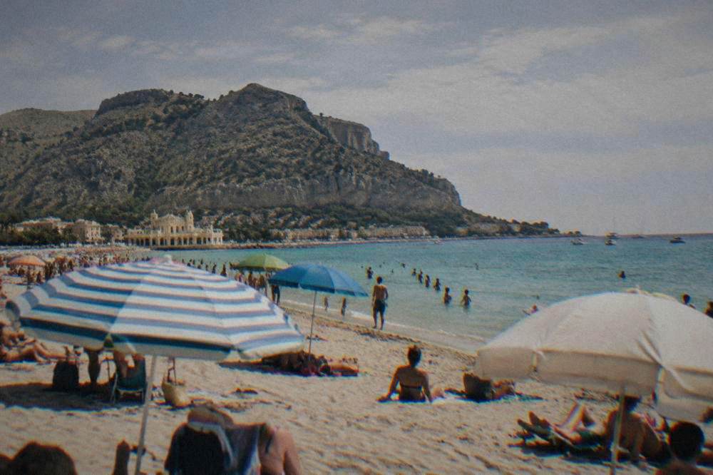 A crowded sandy beach at Mondello with turquoise water and umbrellas on a summer day