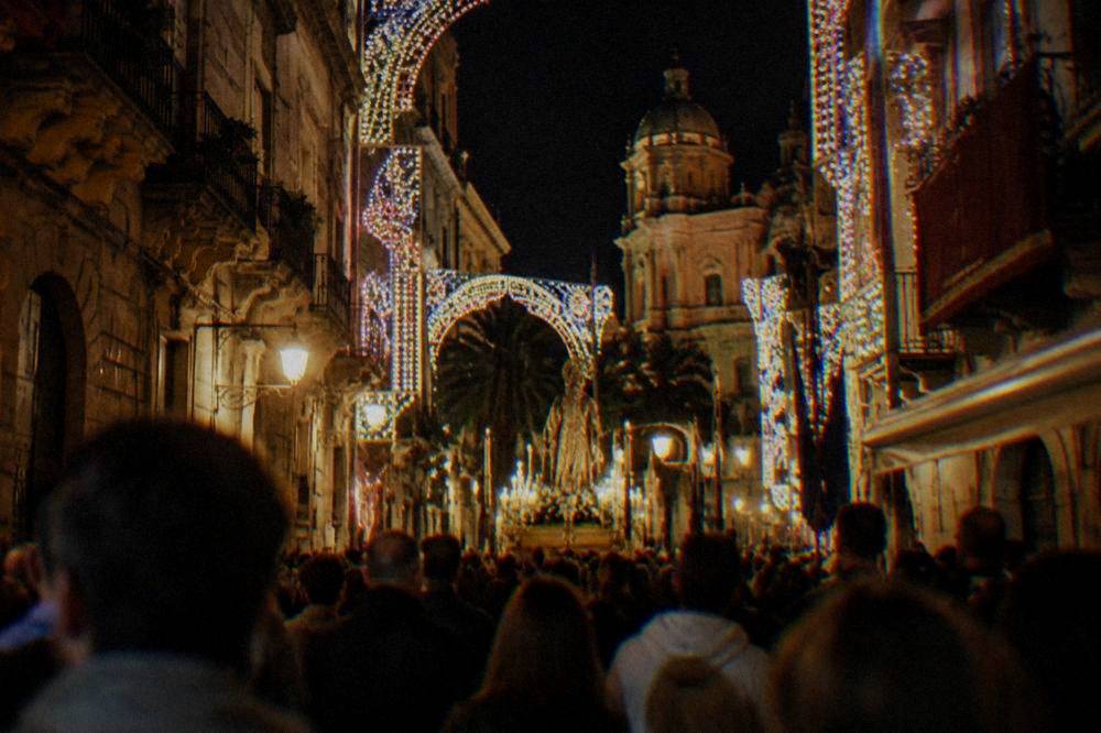 A festive street in Palermo at night with lights and a procession crowd