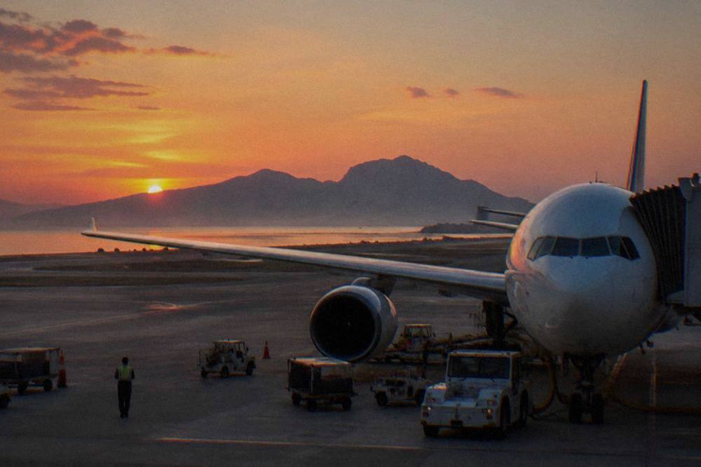 A wide-body aircraft at a gate with ground crew working on the apron at dusk