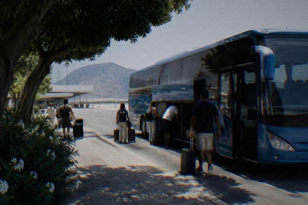 A blue airport coach parked at a kerb with passengers loading luggage