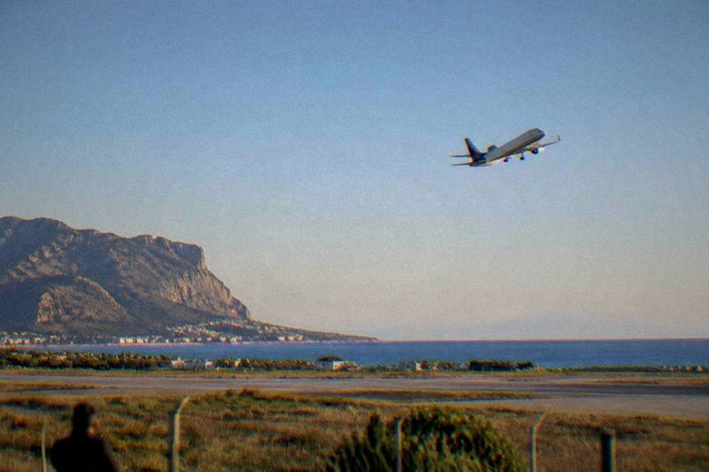 An aircraft climbing into a clear sky above a Mediterranean coastline after takeoff