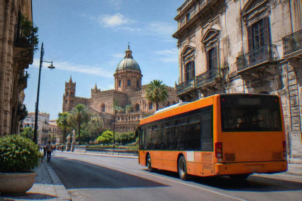 A Palermo street with an orange AMAT bus passing historic buildings