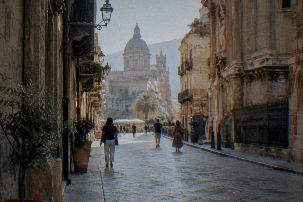 People walking along a sunlit Palermo street lined with historic buildings
