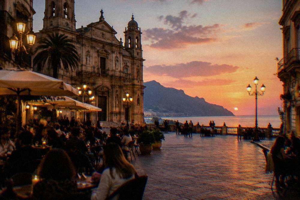 A lit piazza in central Palermo with people gathered at outdoor tables in the evening