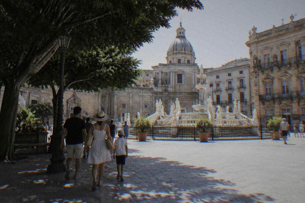 A family walking through a Palermo square with a fountain and historic facades