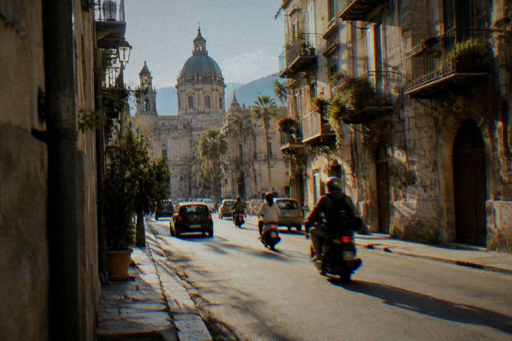 Scooters and small cars moving along a narrow street in the old centre of Palermo