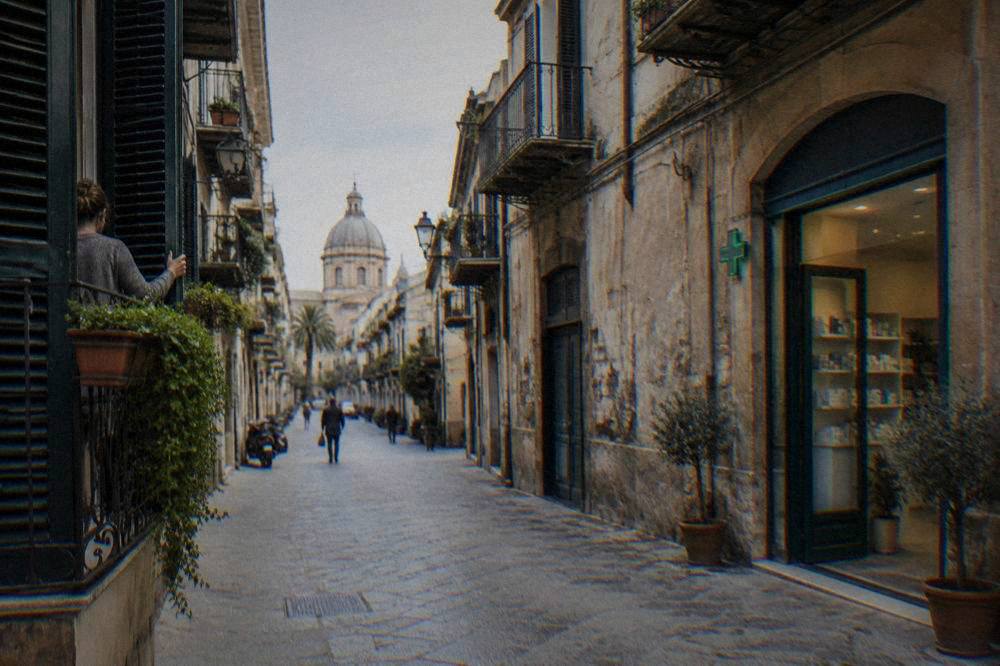 A quiet morning street in Palermo with shutters opening and a pharmacy doorway