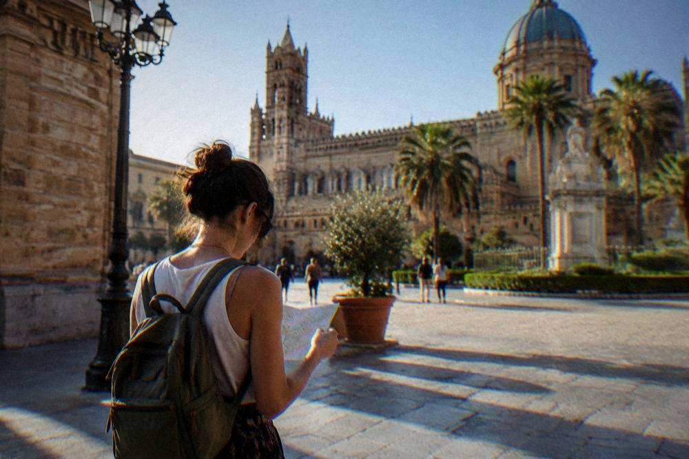 A visitor with a small backpack looking at a map in a sunny Palermo square