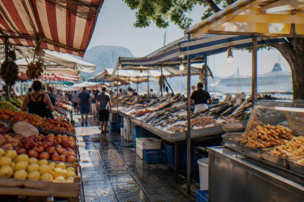 A busy Palermo market street in the morning with stalls of fruit, fish and fried food under striped awnings