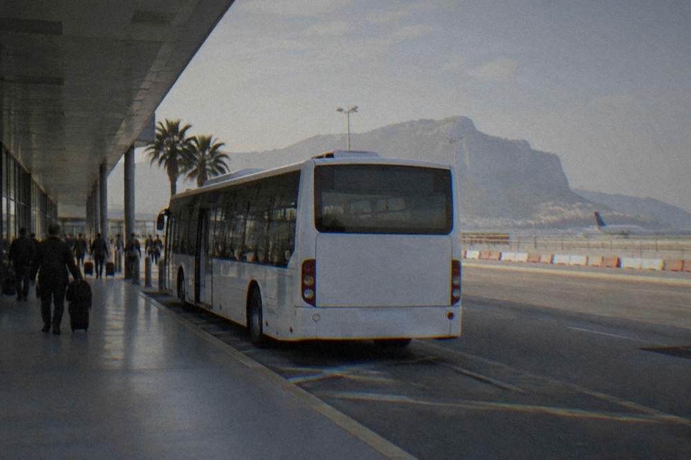 A white airport bus parked at a kerb outside Palermo airport terminal