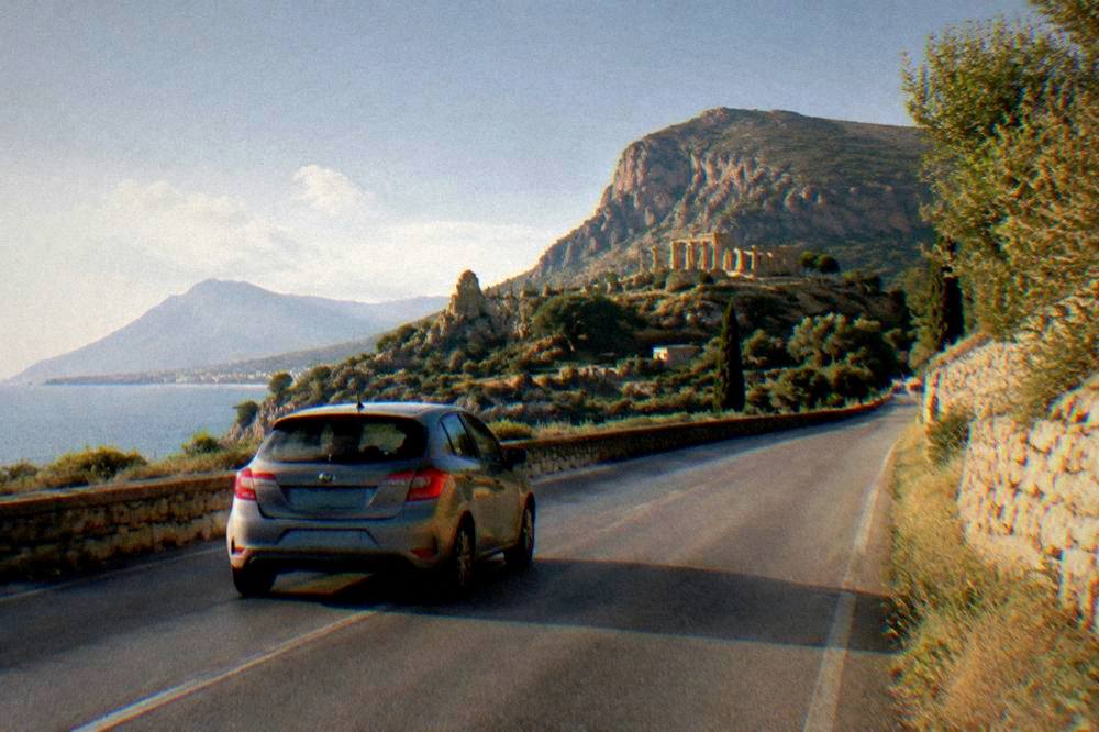 A hire car on an empty Sicilian road with hills and ancient ruins in the distance