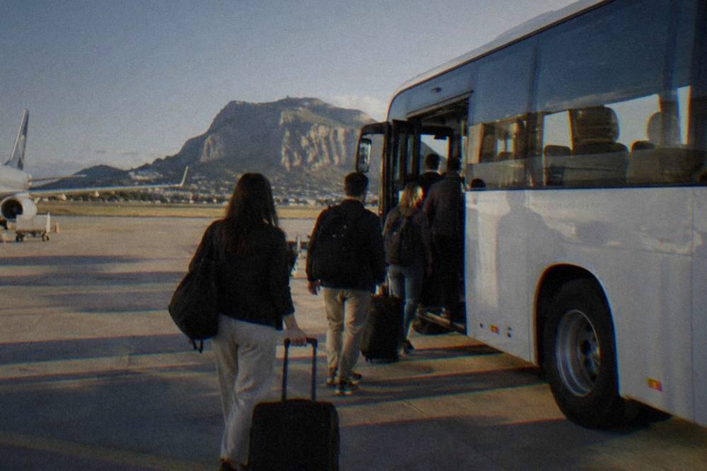 Passengers boarding a white airport coach at Palermo Airport with luggage