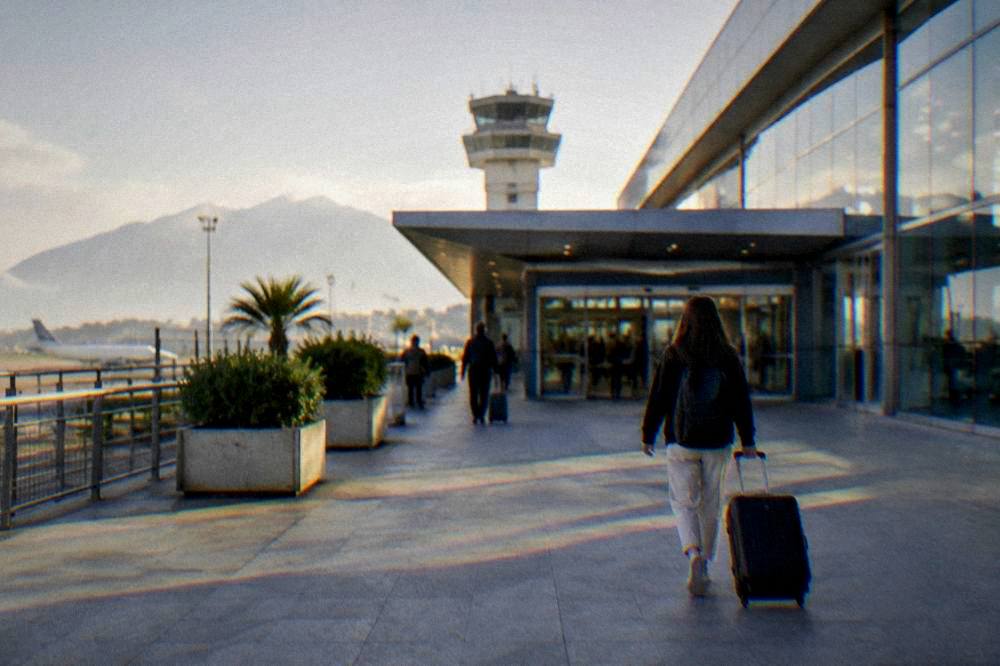 A traveller with a suitcase walking toward the departures entrance of Palermo Airport in morning light