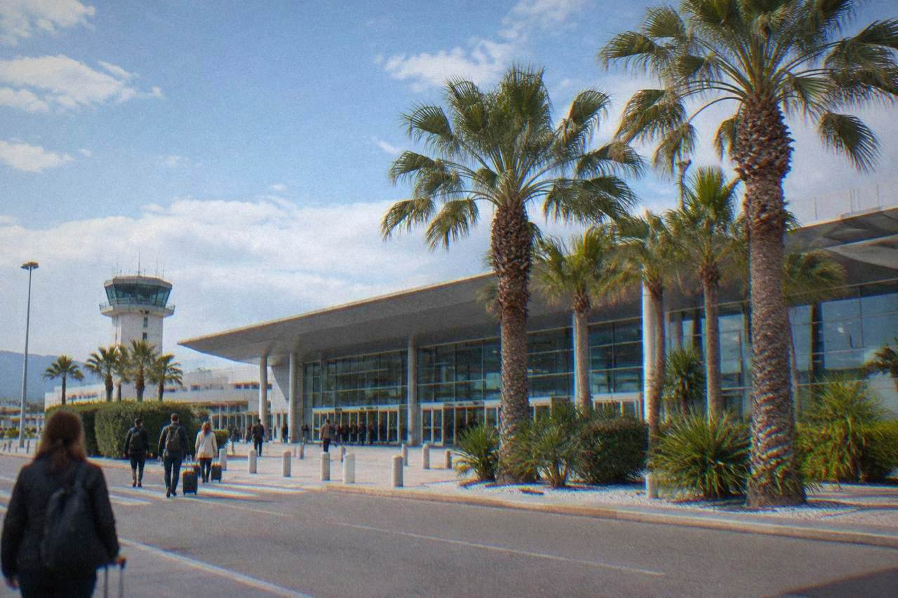 A modern airport terminal building under a bright blue sky with palm trees near the entrance