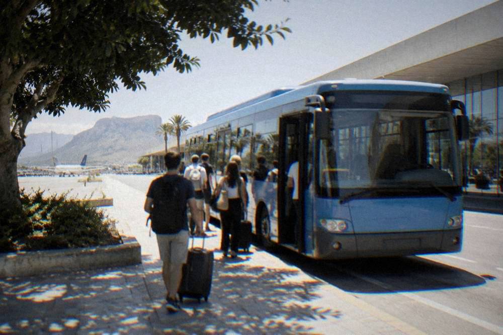 A blue airport shuttle bus parked at a kerb outside a terminal with passengers boarding