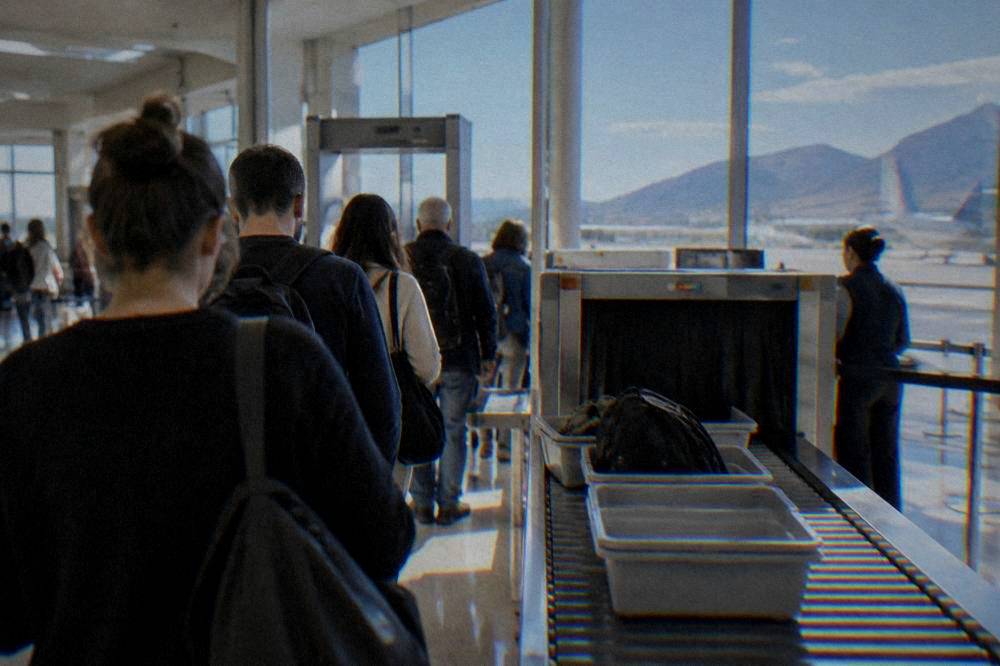 A queue of travellers at an airport security checkpoint with trays on the belt