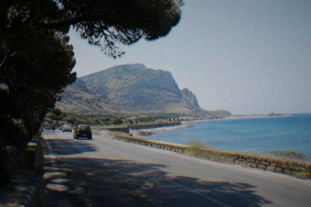 A view of a Sicilian coastal road with the sea on one side and hills on the other